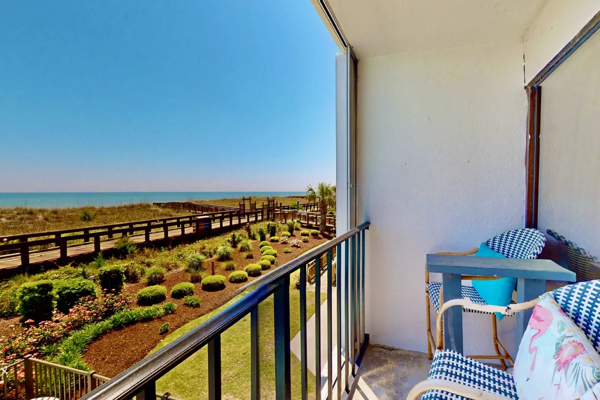 A peaceful exterior balcony scene overlooking a lush garden and sweeping ocean view. Comfortable seating on the balcony invites guests to relax while watching sunrises, fireworks, or simply enjoying the tranquil ambiance just outside their door.