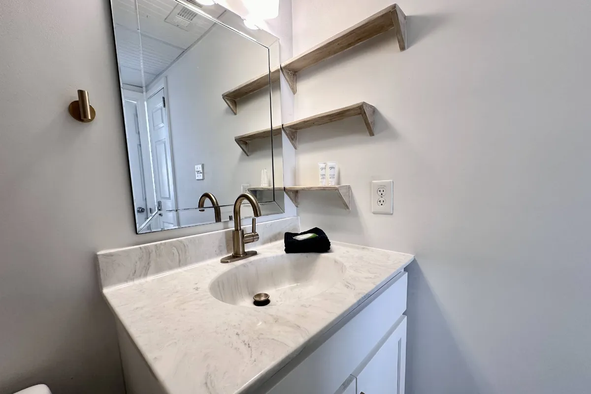 A stylish bathroom with a marble countertop, brushed gold faucet, mirror, and neatly organized wooden shelves. The setting exudes a serene and spa-like atmosphere, ideal for self-care and relaxation.