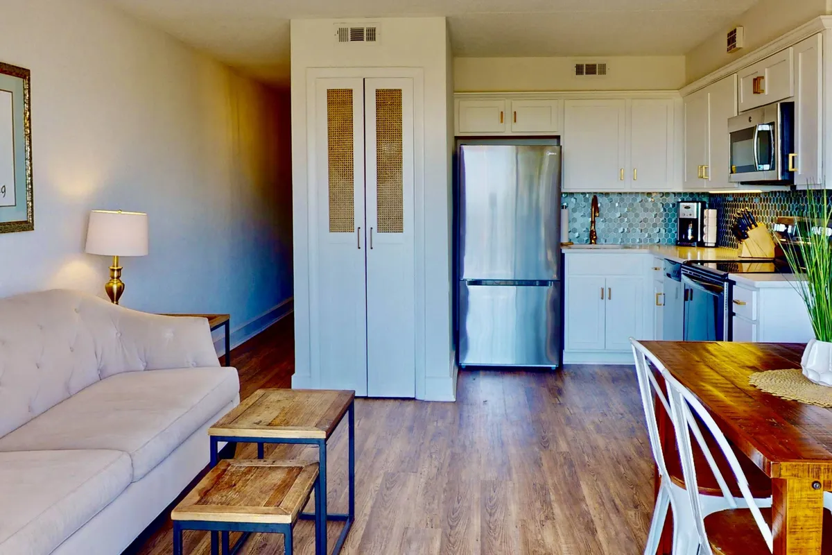 An open-plan interior combines a cozy sofa, a welcoming dining table set for a meal, visible kitchen appliances, and tasteful wall art. The scene feels lived-in and perfect for both intimate dinners and casual gatherings with friends or family, highlighting the seamless flow between spaces.