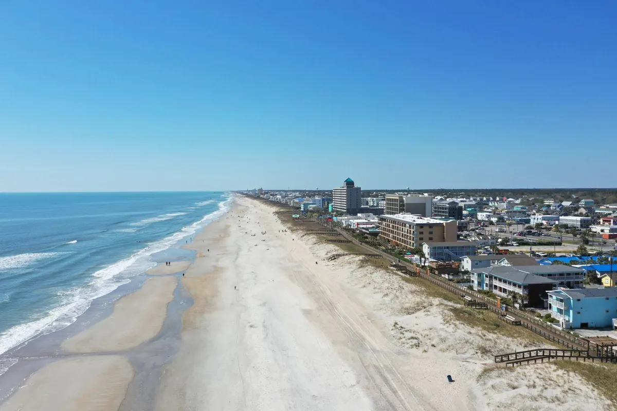 A wide, inviting view of the expansive sandy beach, rolling ocean waves, a vibrant boardwalk, and the town skyline. This scene immerses viewers in the destination’s relaxed coastal lifestyle and highlights the seamless connection between the beach, boardwalk, and town activities.