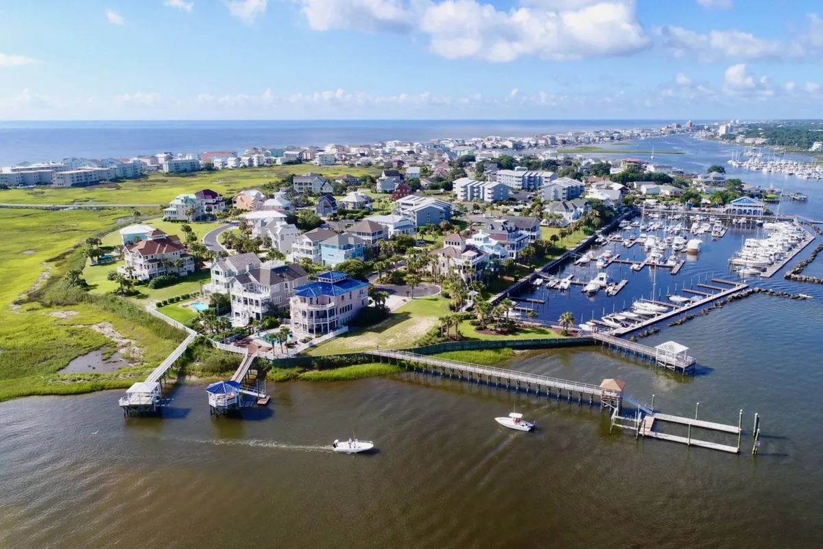 A lively marina scene featuring boats docked along the waterfront, surrounded by grassy areas and residential homes. The inviting docks and boats are central, suggesting opportunities for boating, fishing, and waterfront exploration. The atmosphere is relaxed yet active, reflecting the vibrancy of coastal living.